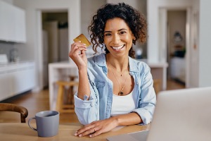 Woman smiling at computer with credit card in hand 